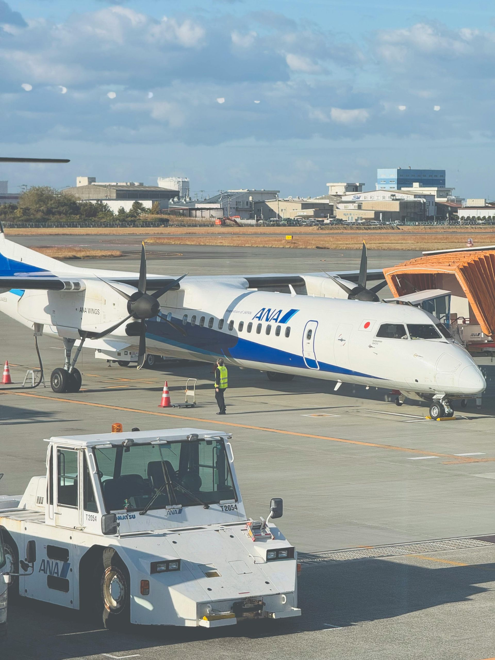 White and blue airplane parked on tarmac at an airport. A ground crew worker is near the plane.