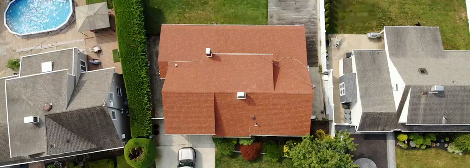 An aerial view of a house with a red roof and a pool in the background.