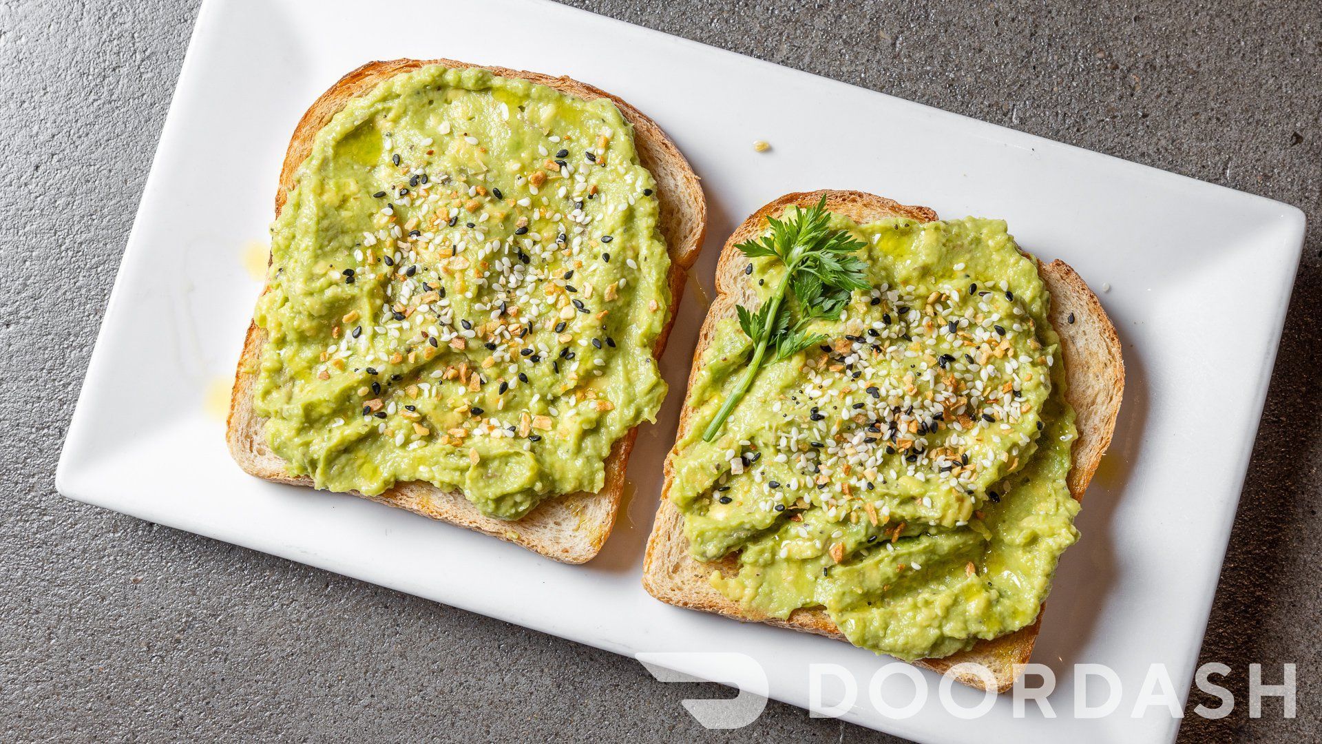 Two slices of toast with guacamole on them on a white plate.