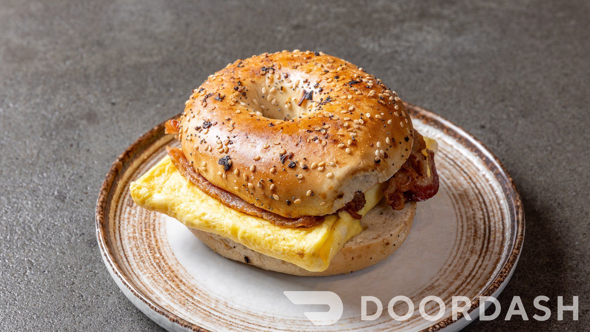 A bagel with eggs and bacon on a plate.