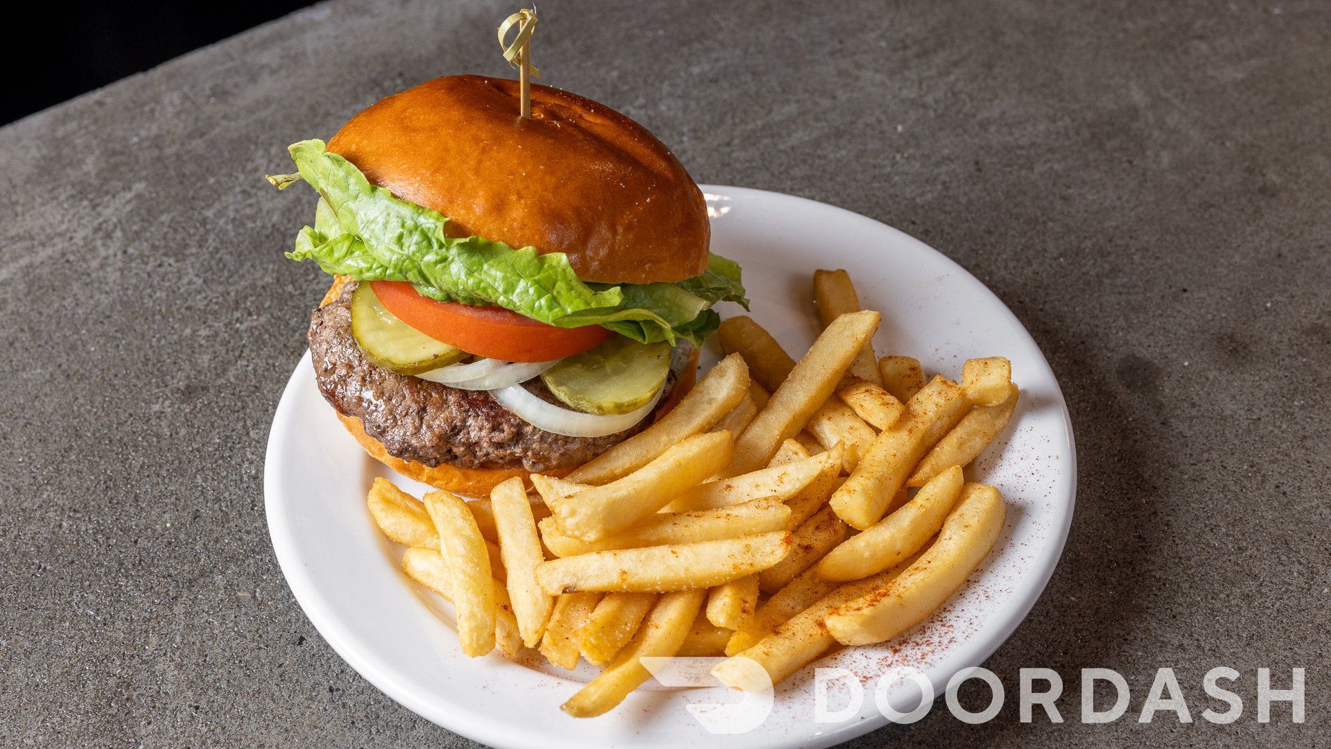 A hamburger and french fries on a white plate on a table.
