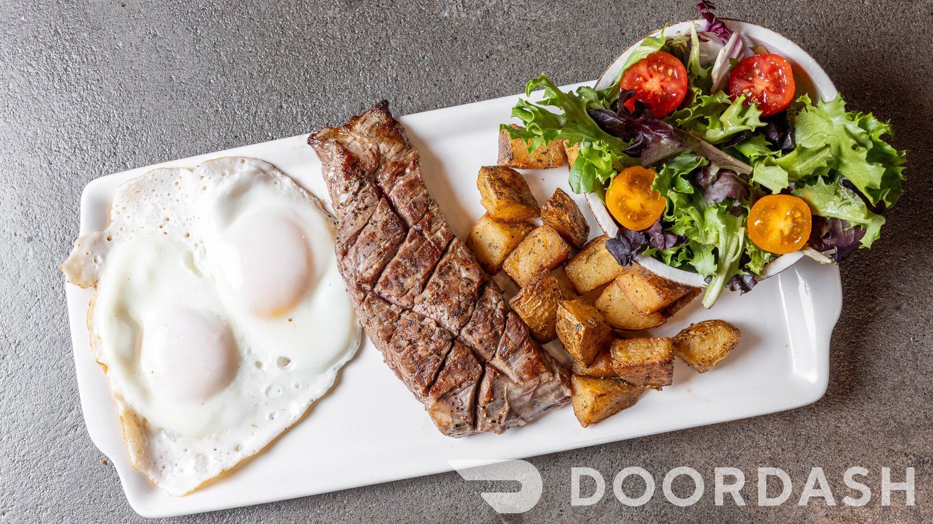 A white plate topped with steak , eggs , potatoes and a salad.
