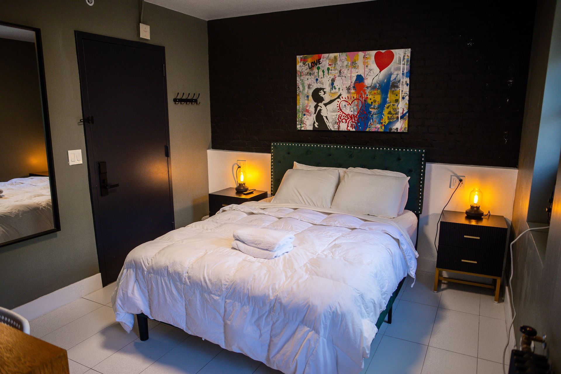 A hotel room with a bed , nightstand , mirror and painting on the wall.