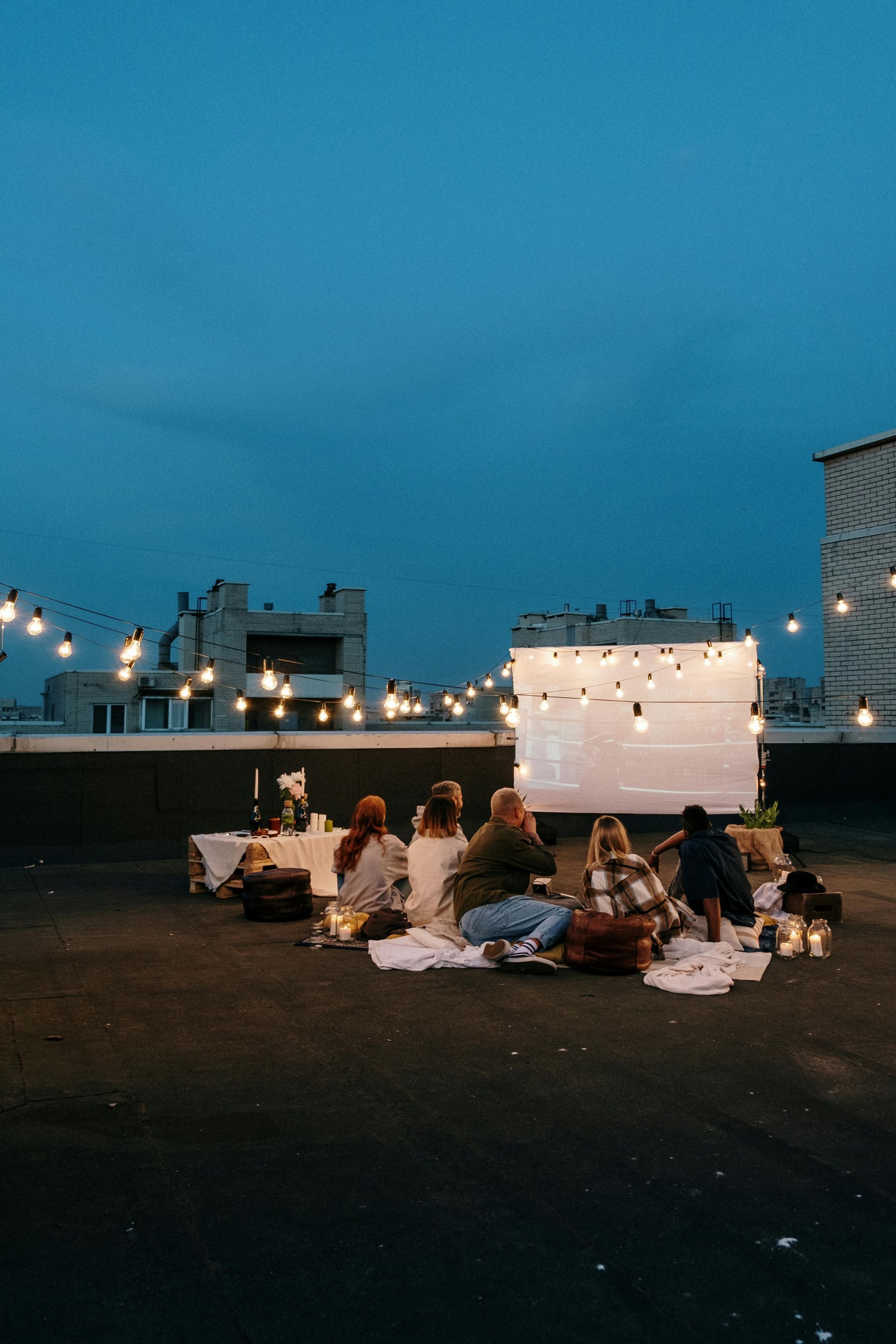 A group of people are sitting on the ground on a rooftop watching a movie.