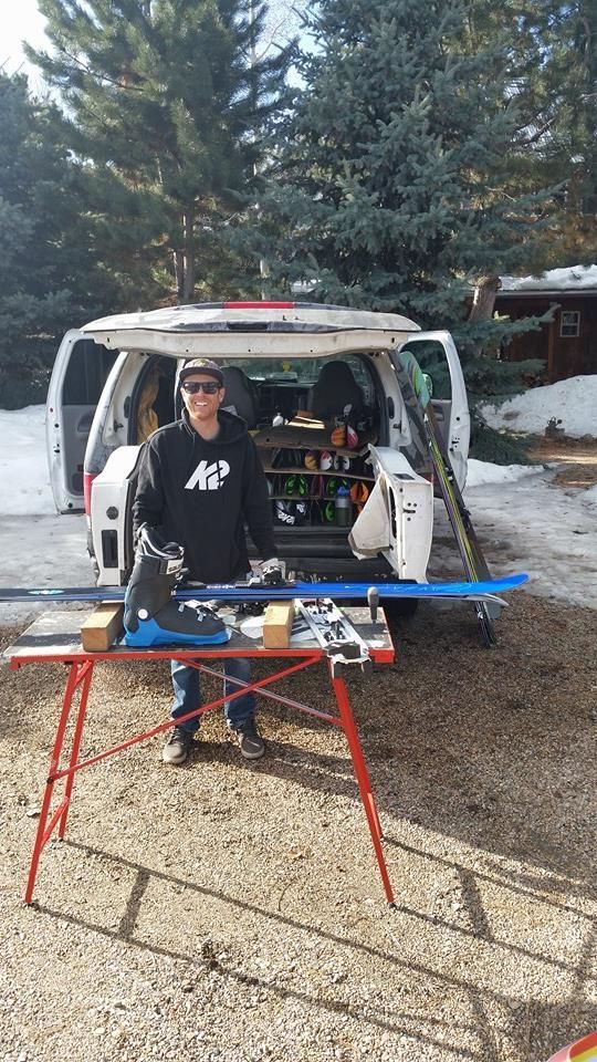 A man is standing in front of a van with skis in the back.