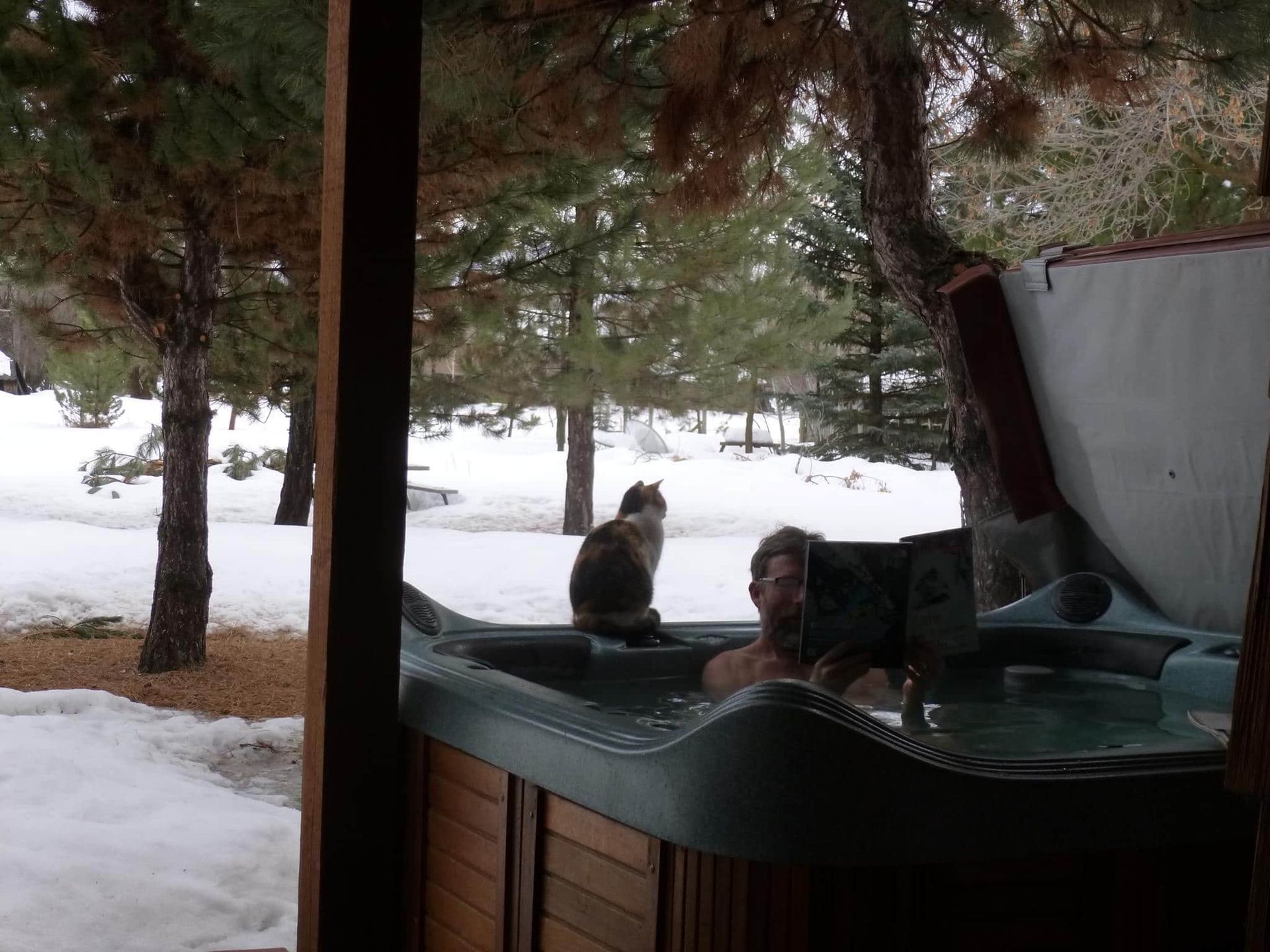 A man and a cat are sitting in a hot tub in the snow