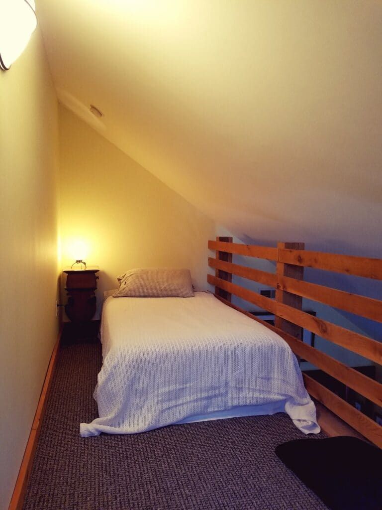 A small bedroom with a single bed and a wooden railing.