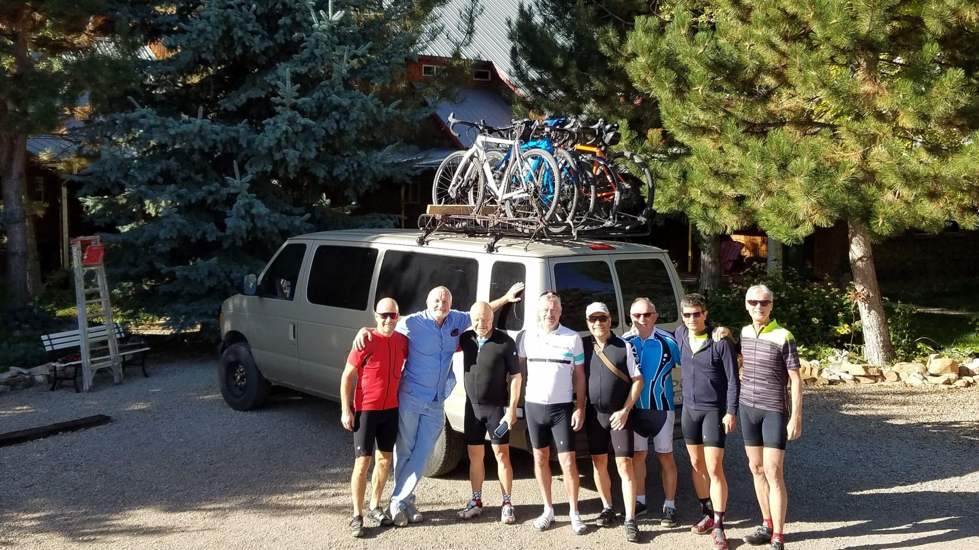 A group of people standing in front of a van with bikes on the roof.