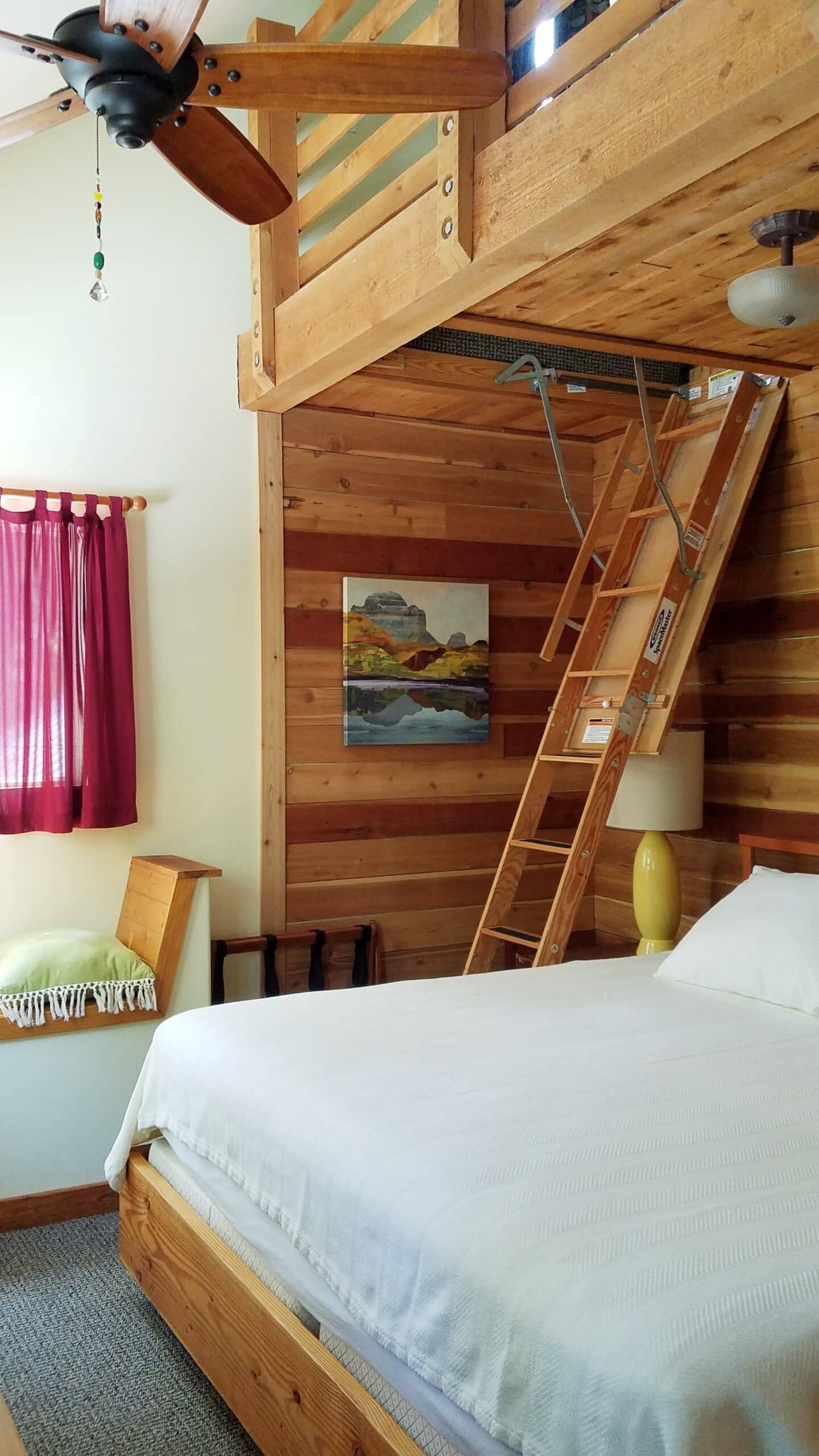 A bedroom with a bed and a ladder leading to the loft.