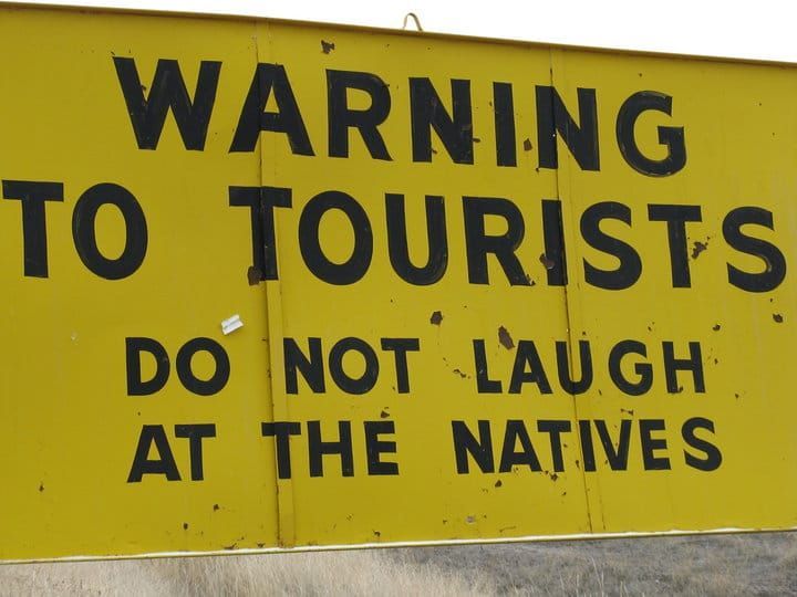 A yellow sign that says warning to tourists do not laugh at the natives