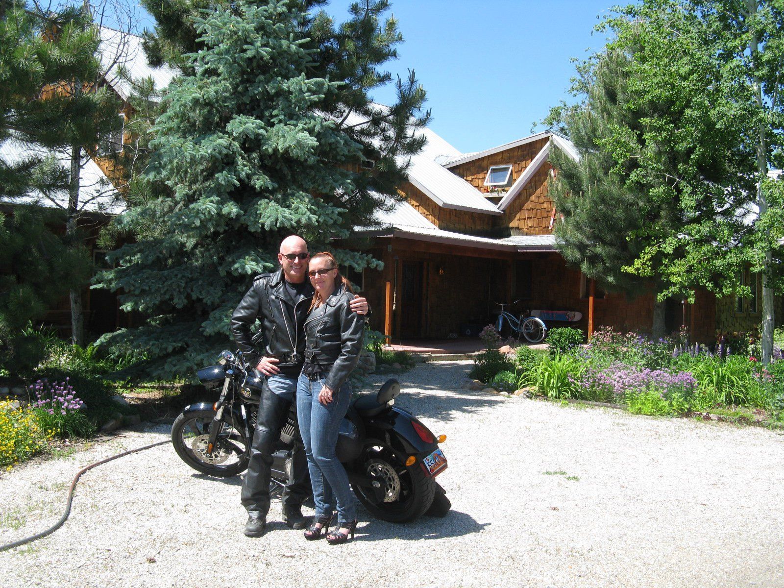 A man and woman standing next to a motorcycle in front of a house