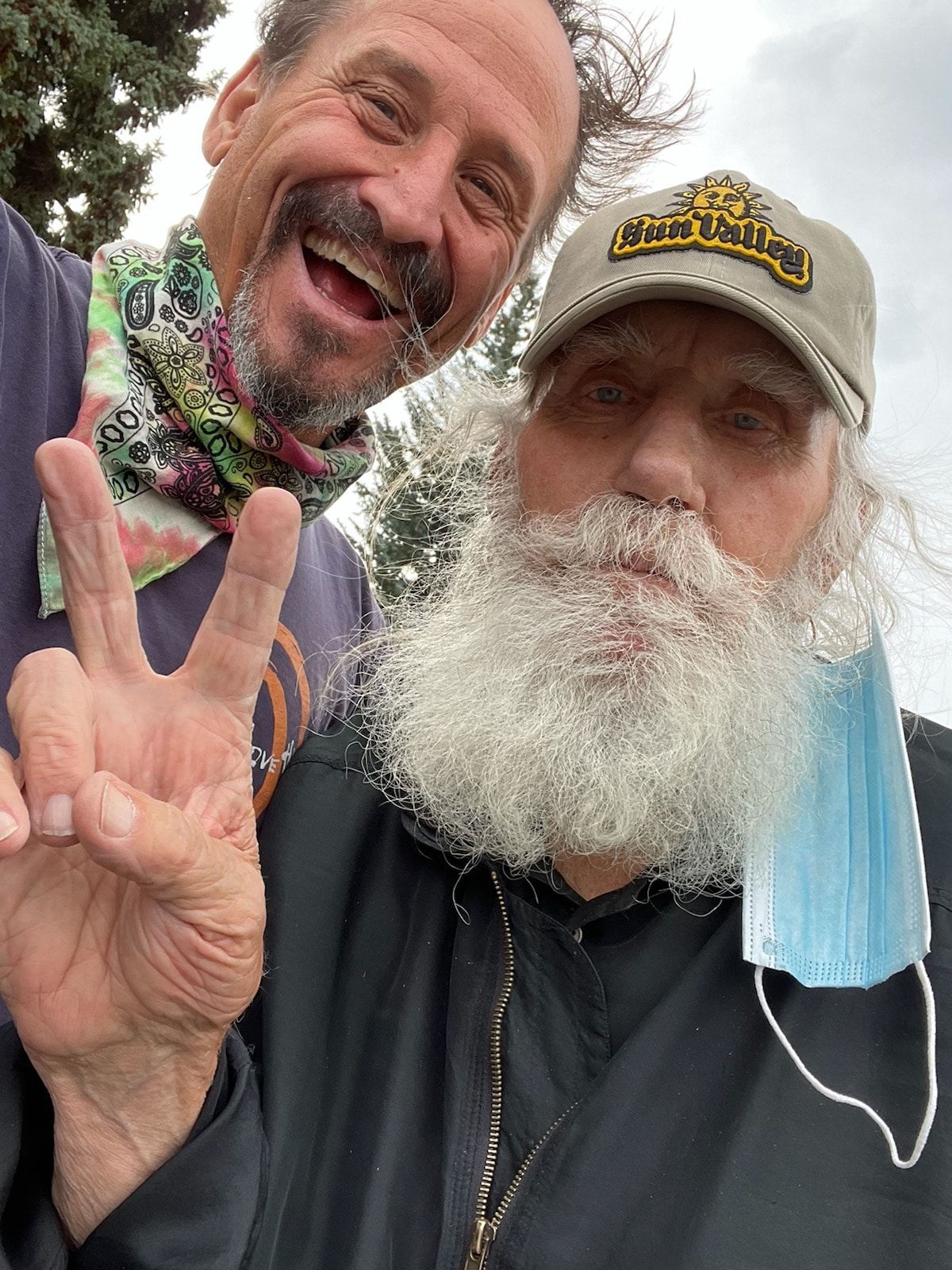 A man with a beard is giving a peace sign next to another man.