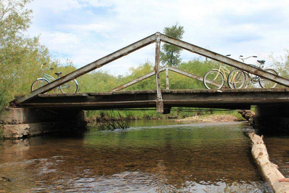 Two bicycles are parked under a bridge over a river.