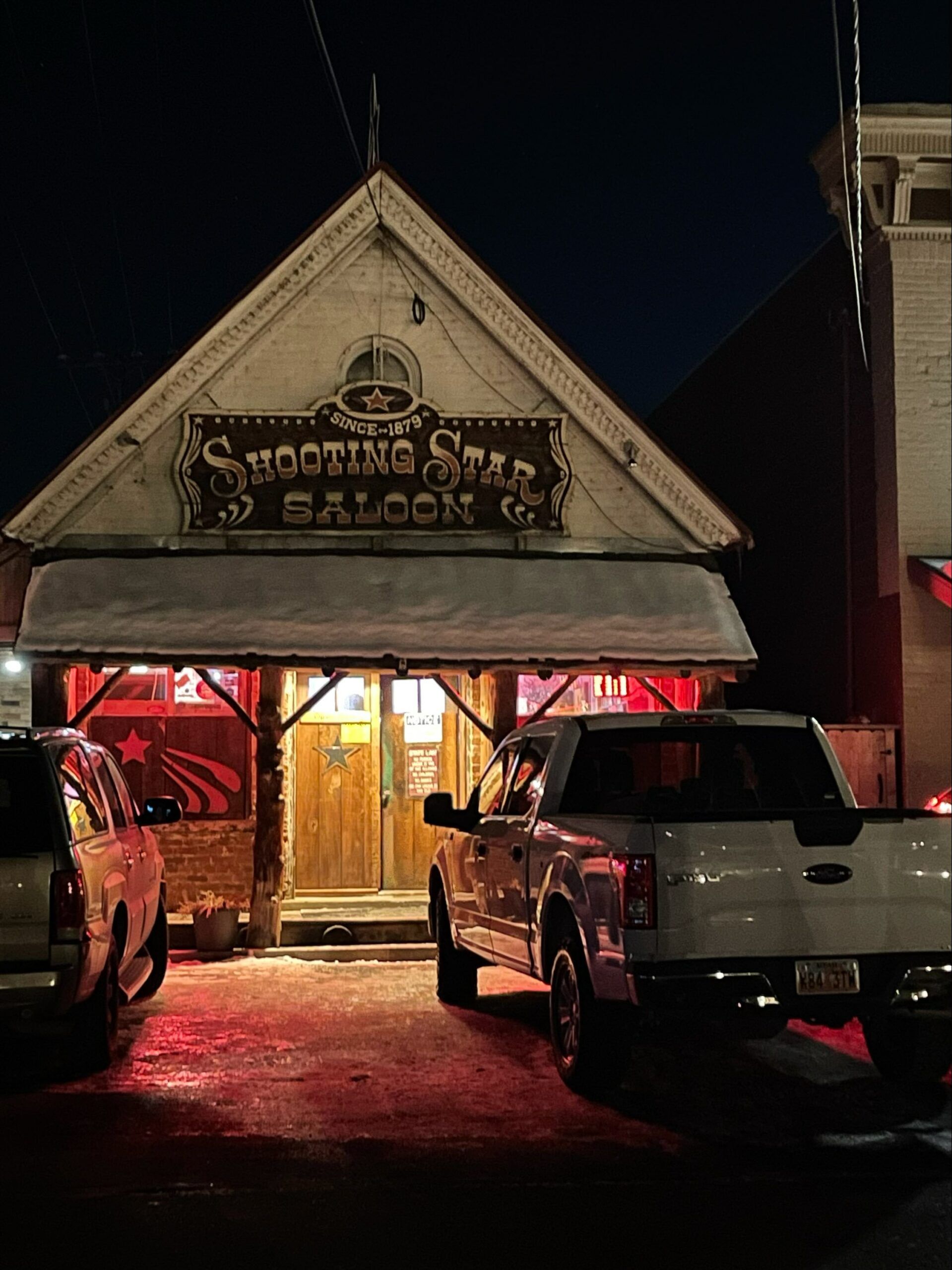A truck is parked in front of a saloon at night