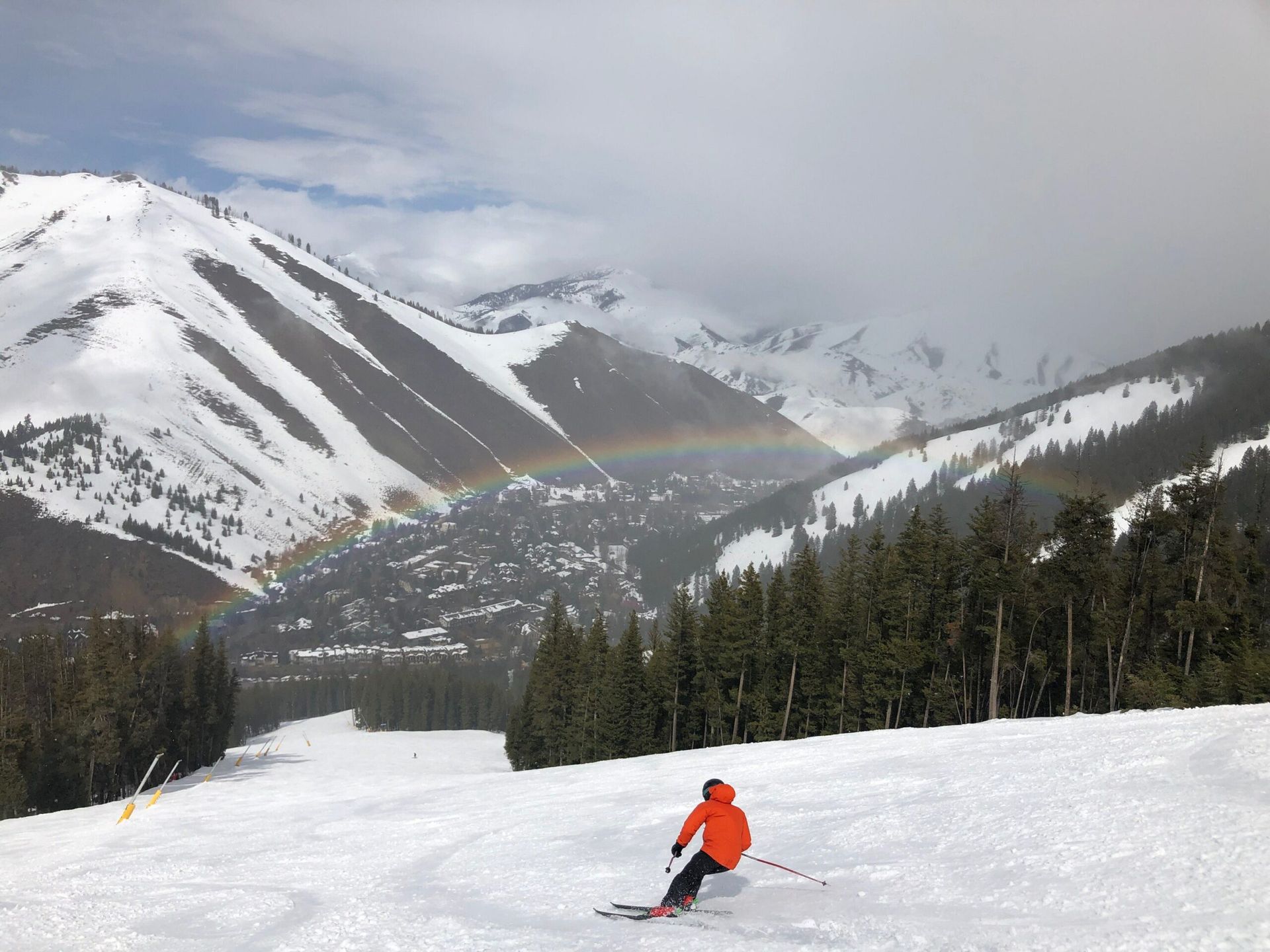 A person is skiing down a snowy mountain with a rainbow in the background.