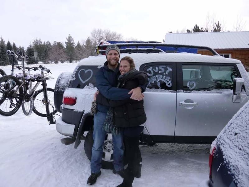 A man and woman hugging in front of a car that says just married