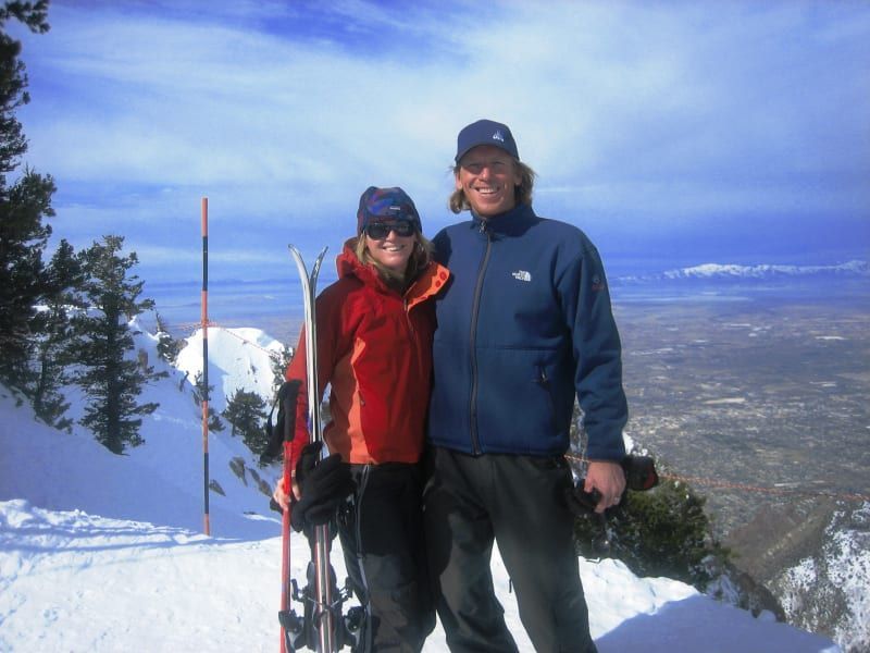 A man wearing a north face jacket stands next to a woman holding skis