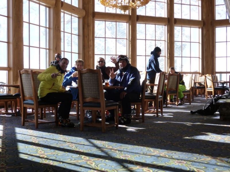 A group of people are sitting at tables in a room with lots of windows