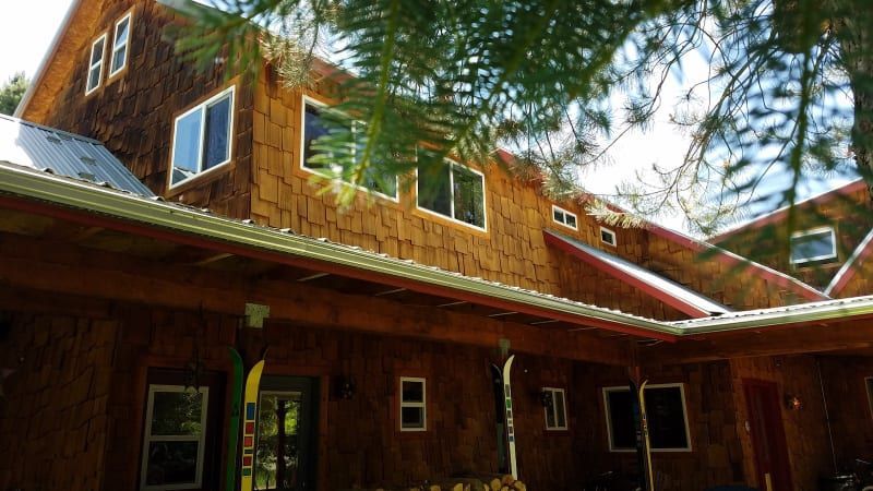 A large wooden house with a red roof is surrounded by trees.
