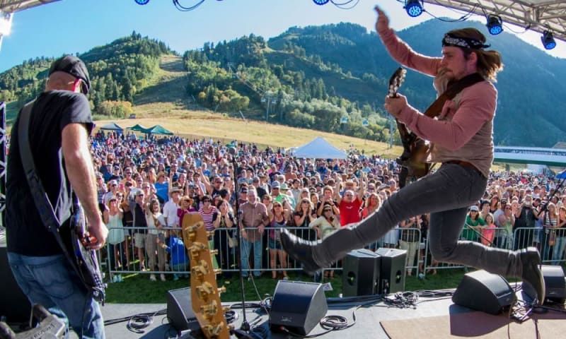 A man is jumping in the air while playing a guitar in front of a crowd.