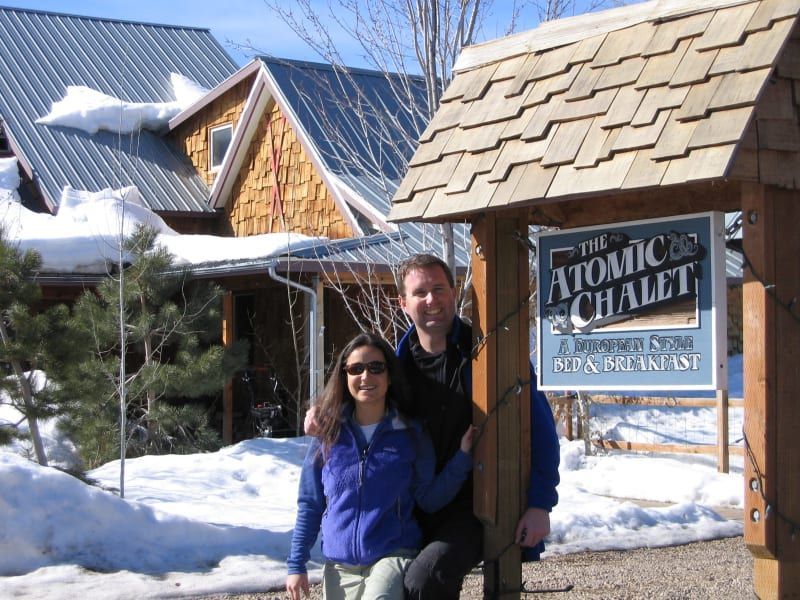 A man and a woman pose in front of a sign for the atomic chalet