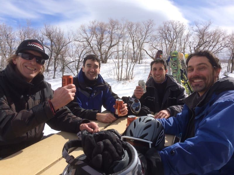 A group of men are sitting at a picnic table in the snow drinking beer