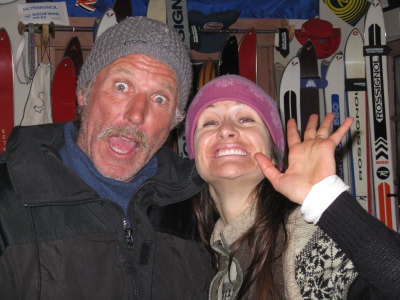 A man and a woman are posing for a picture with skis hanging on the wall behind them