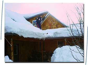 A man is shoveling snow off the roof of a house.
