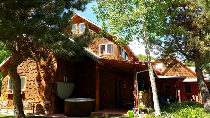 A large wooden house with a hot tub on the porch surrounded by trees.