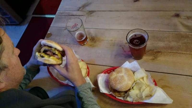 A woman is sitting at a table eating a hamburger and chips.