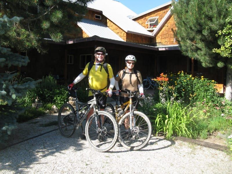 Two people standing next to their bikes in front of a house