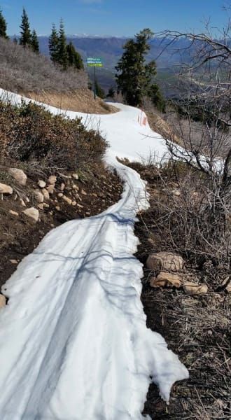 A path covered in snow on a hillside with mountains in the background.