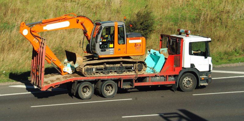 A lorry with a mini digger on the back, travelling down a motorway