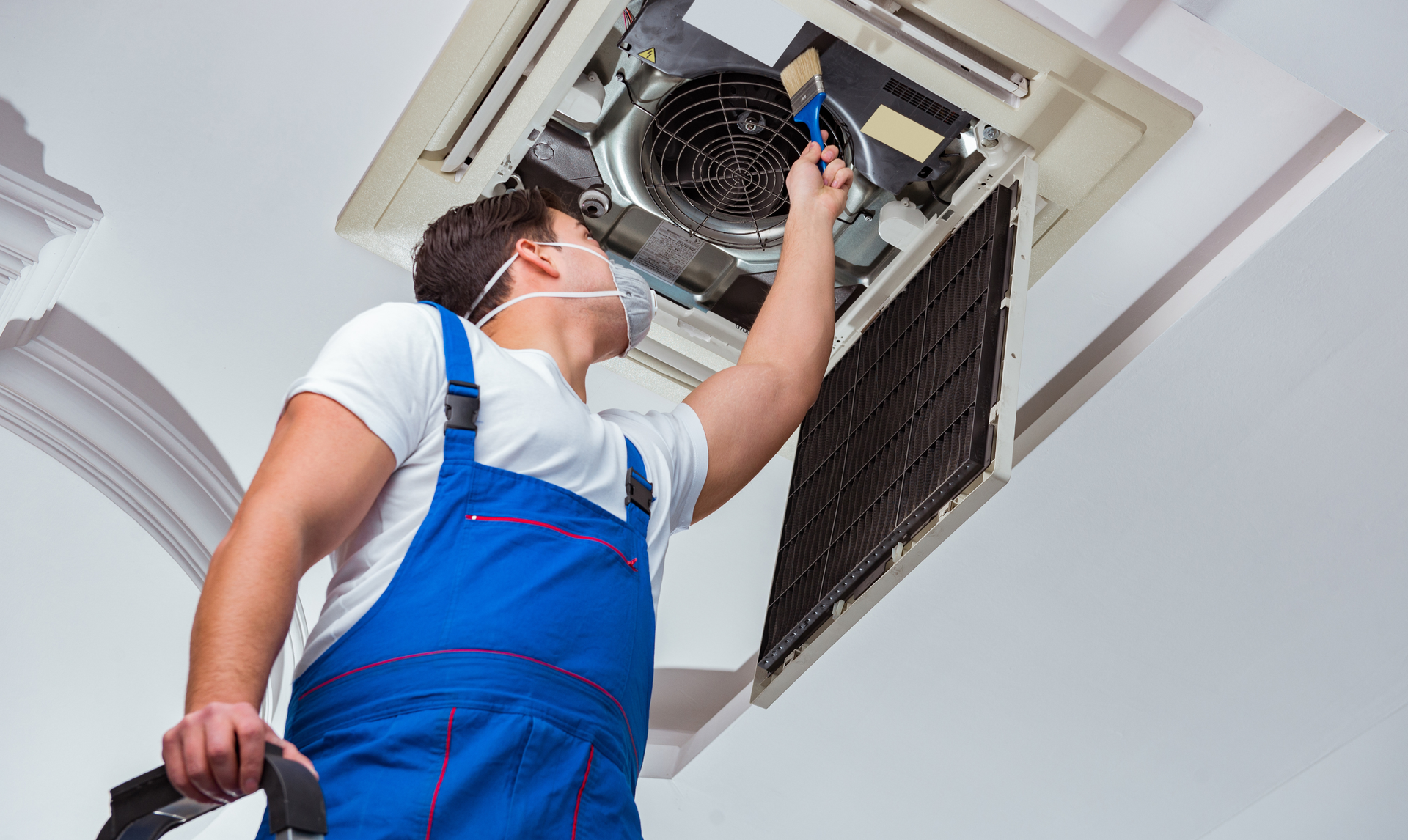 HVAC technician cleaning an air vent on a ceiling with a vacuum and brush.