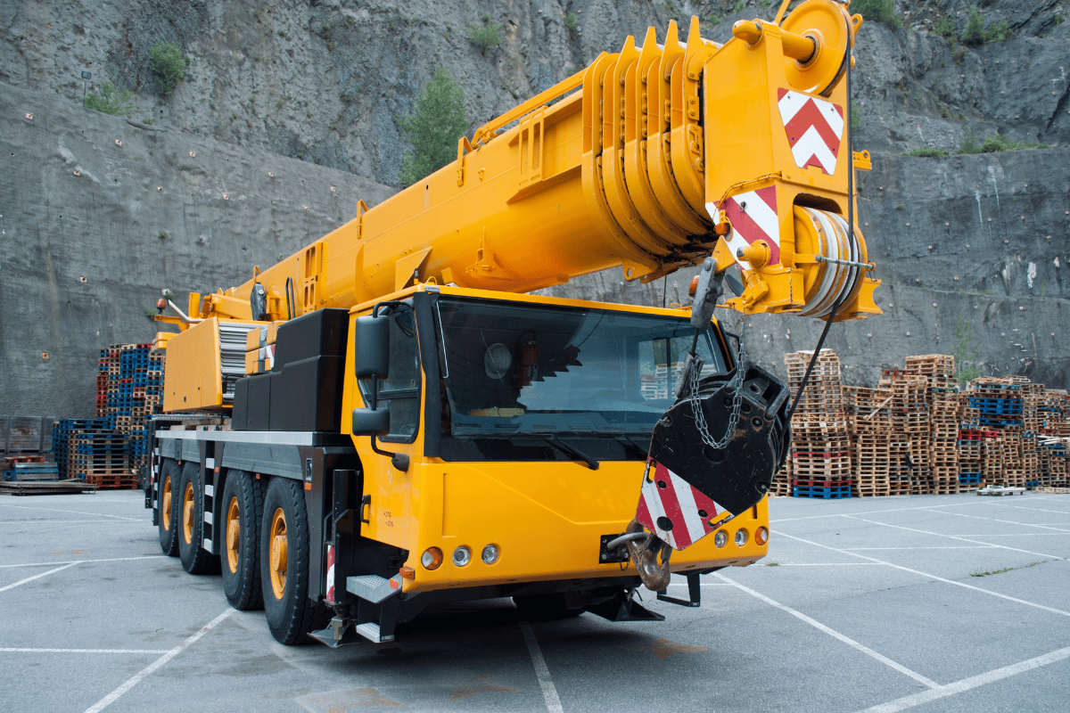 Yellow mobile crane parked, ready for operation.  The setting is outdoors with a rocky hillside.