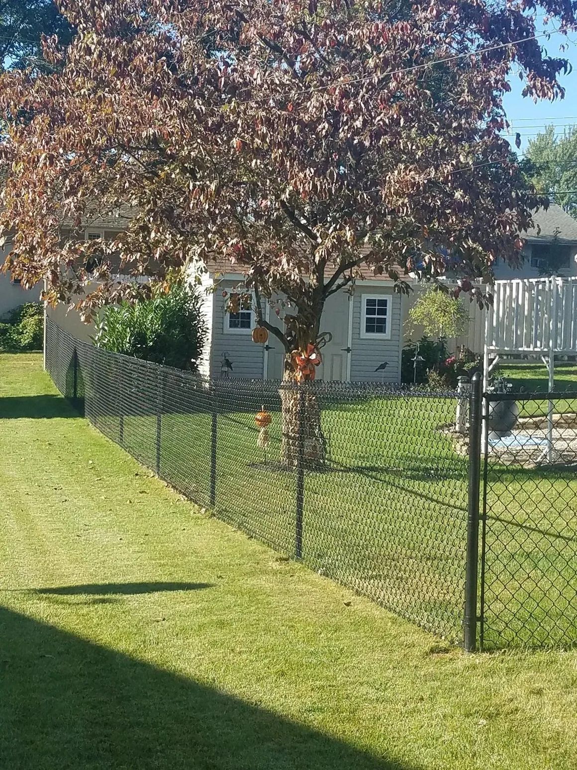 Cross-section of fence post installation. Brown fence post set in concrete; metal post also shown for support.