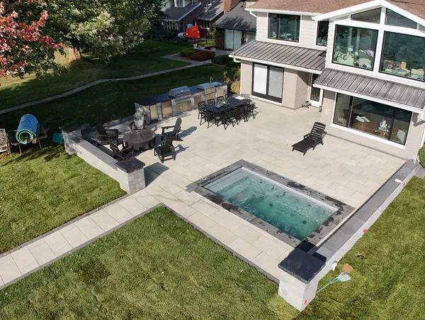 A high-angle view of a backyard patio featuring a rectangular pool, outdoor kitchen, dining area, and lawn.