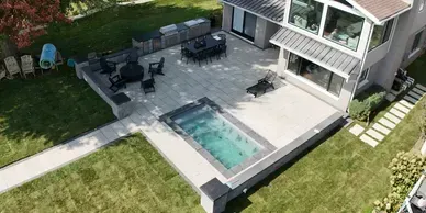 Aerial view of a patio with a rectangular swimming pool, outdoor dining table, fire pit area, and a kitchen counter.