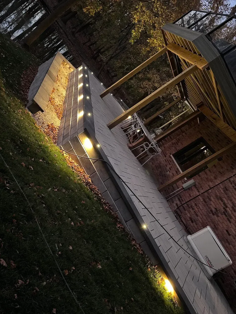 A brick house patio at night illuminated by a string of lights draped over a concrete retaining wall.