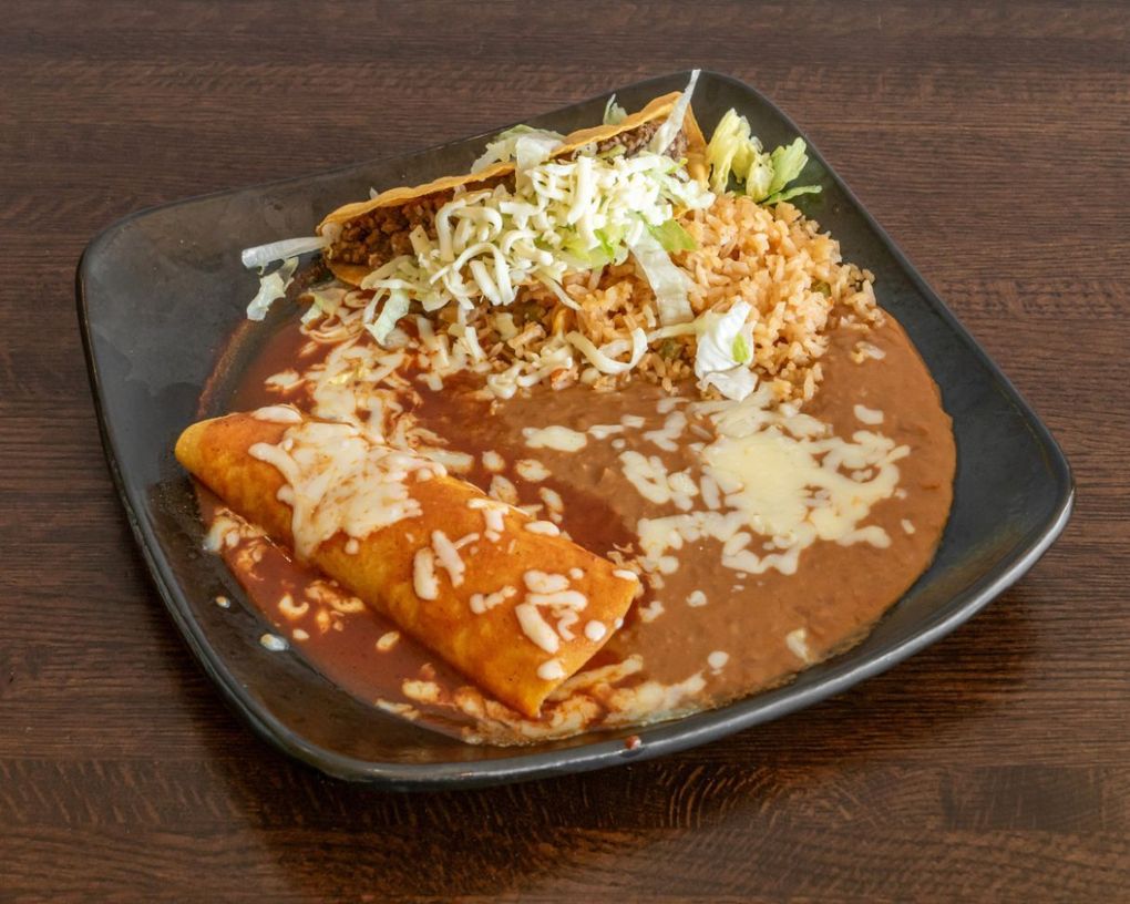 Mexican meal on a black plate with enchiladas, rice, refried beans, and shredded lettuce