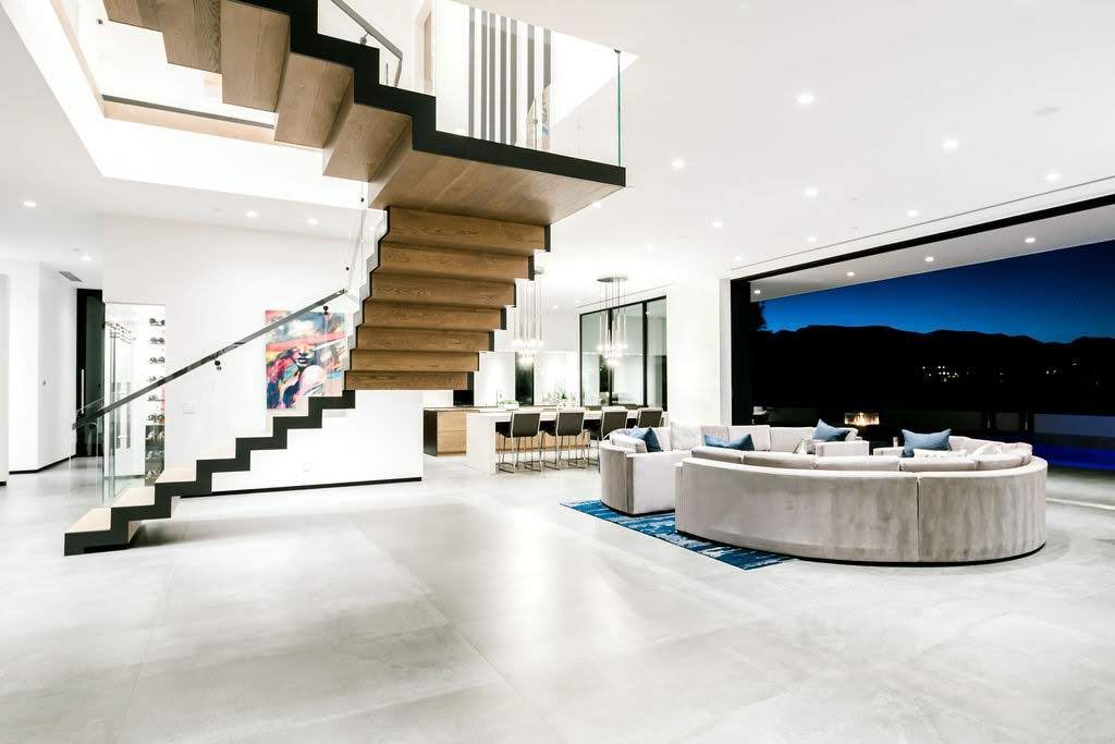Modern home interior: open floor plan with floating staircase, glass railings, and large windows with outdoor view.