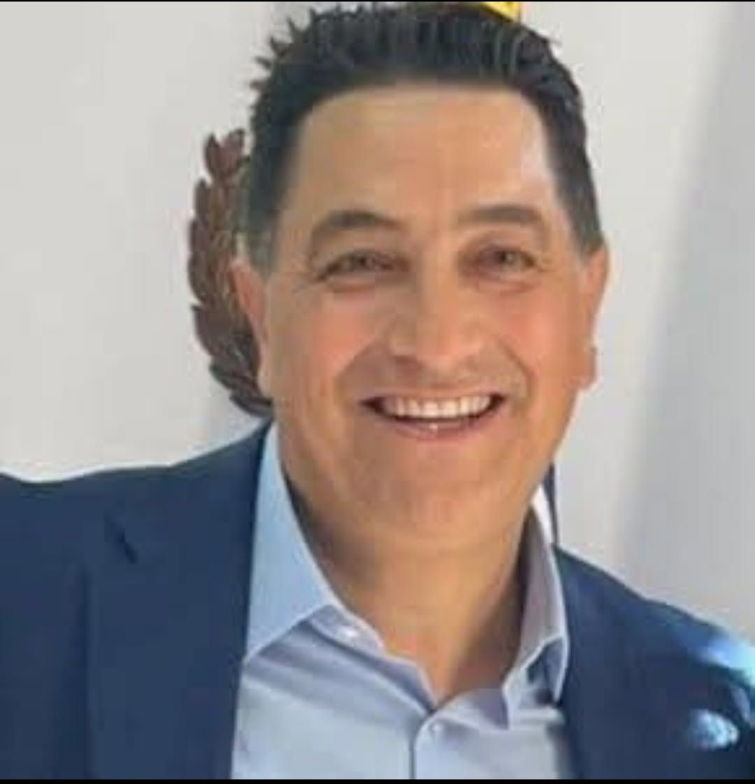 A man in a suit and tie is smiling in front of a flag.