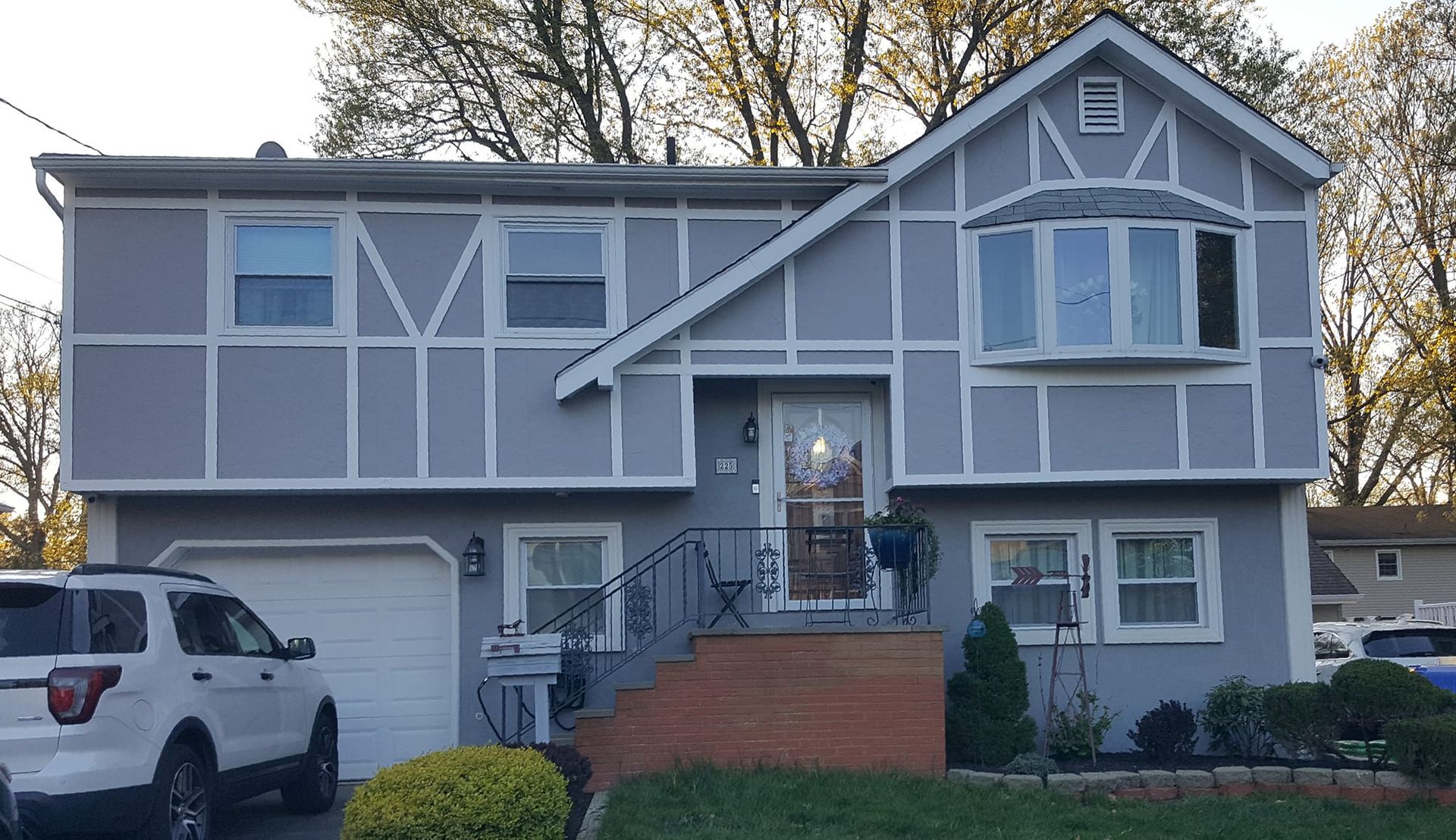 A white suv is parked in front of a gray house.