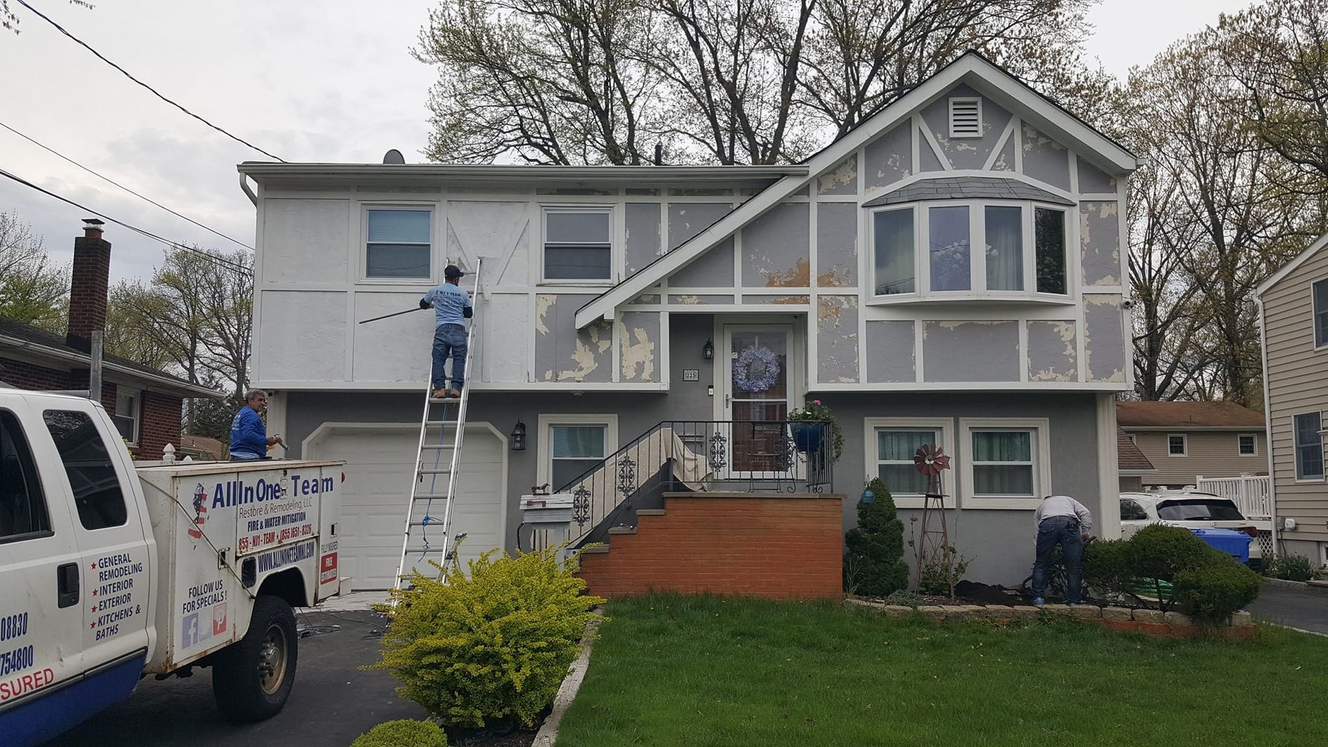 A man on a ladder is painting the side of a house.