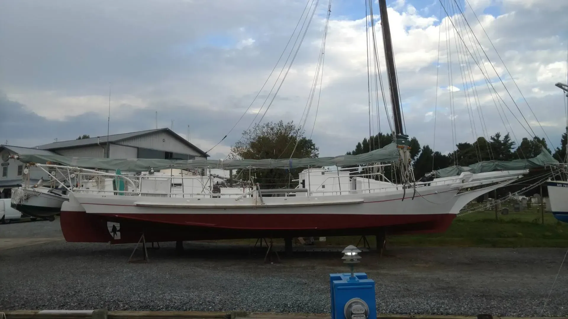 A red and white sailboat is parked in a gravel lot.
