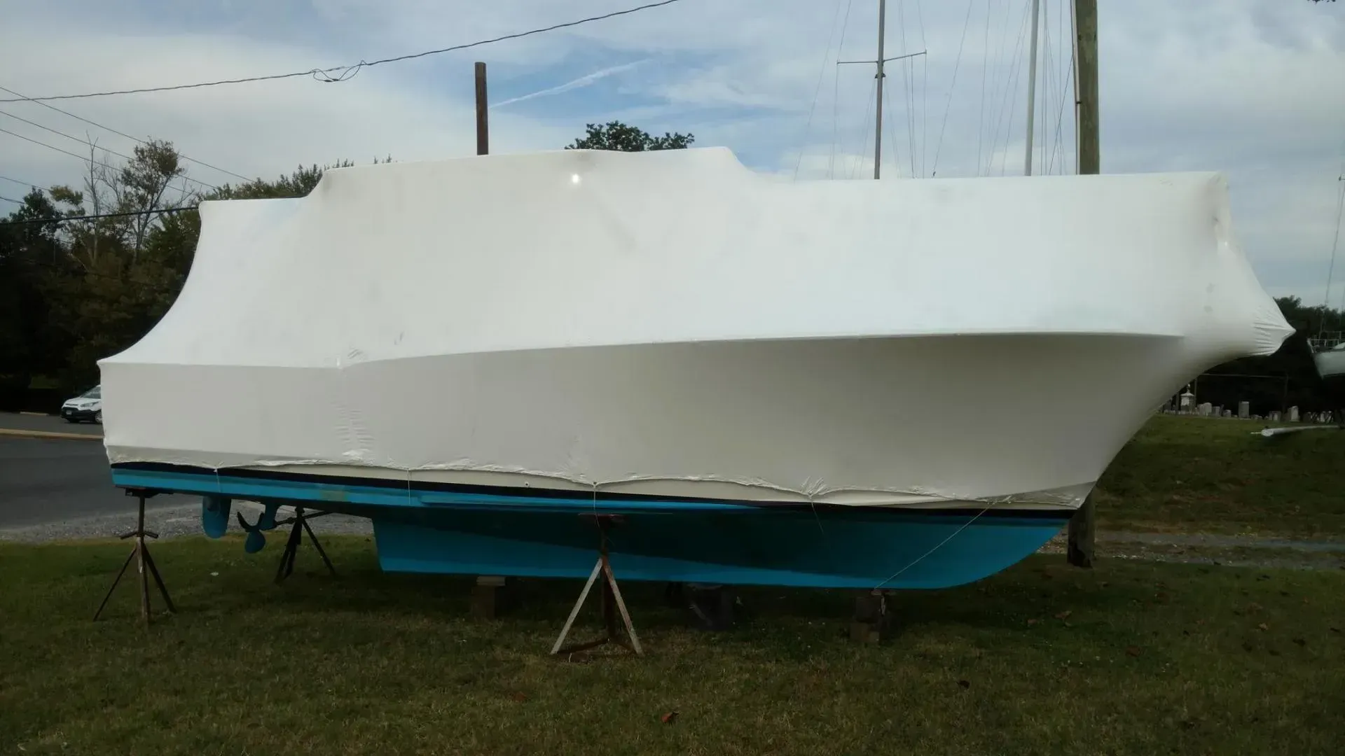 A boat is wrapped in plastic and sitting in the grass