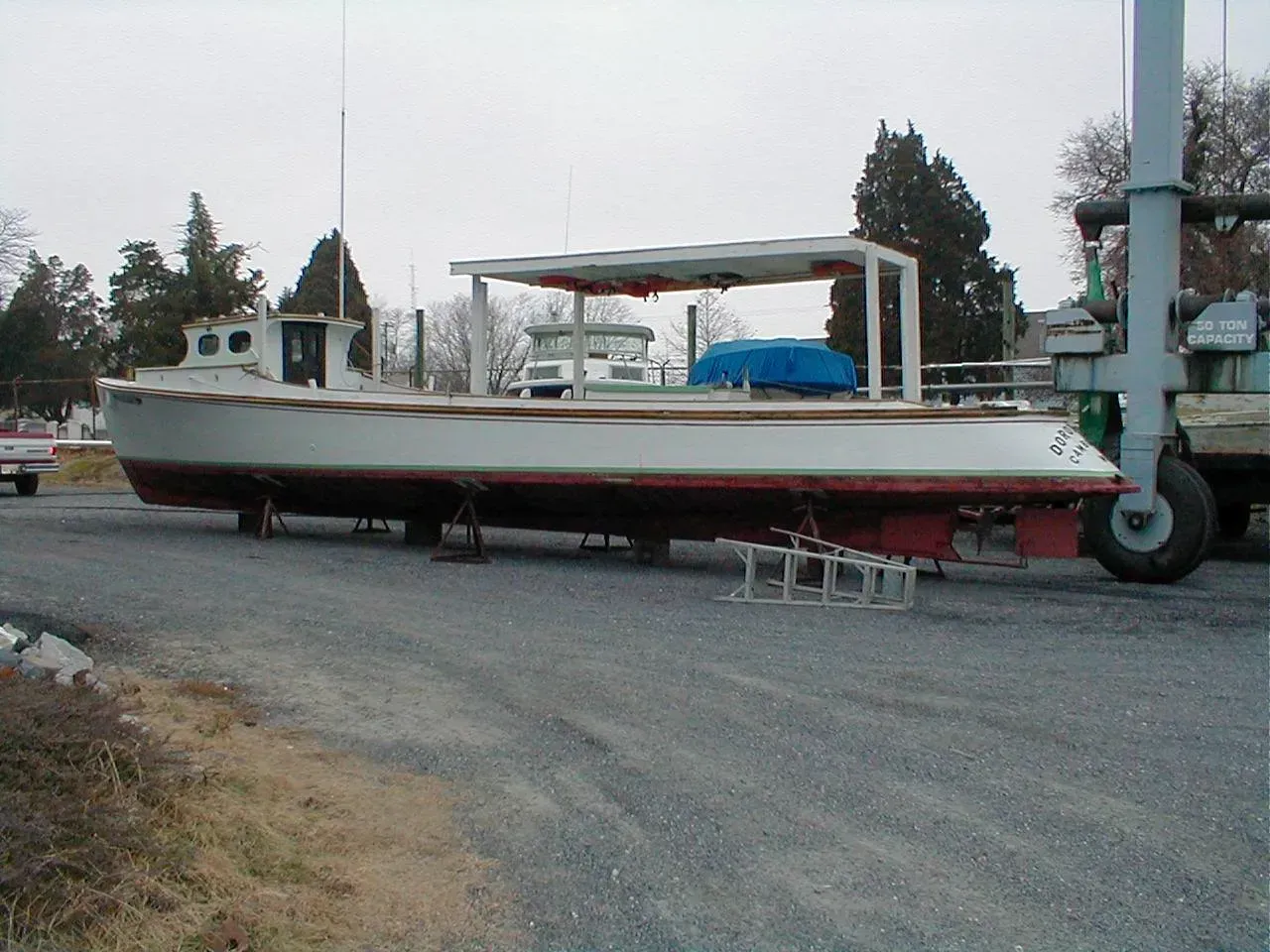 A boat is being lifted by a forklift on a gravel road