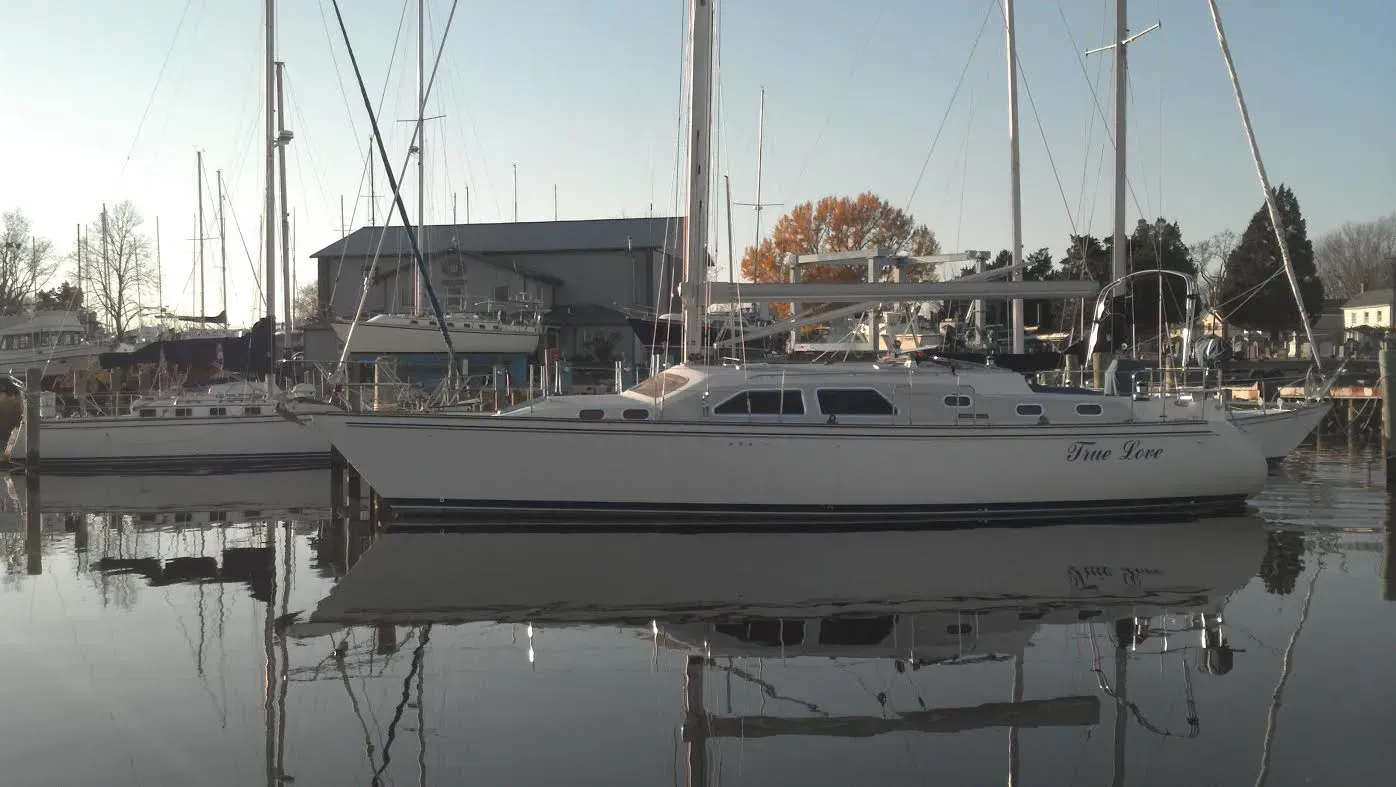 A sailboat is docked in a marina and is reflected in the water.