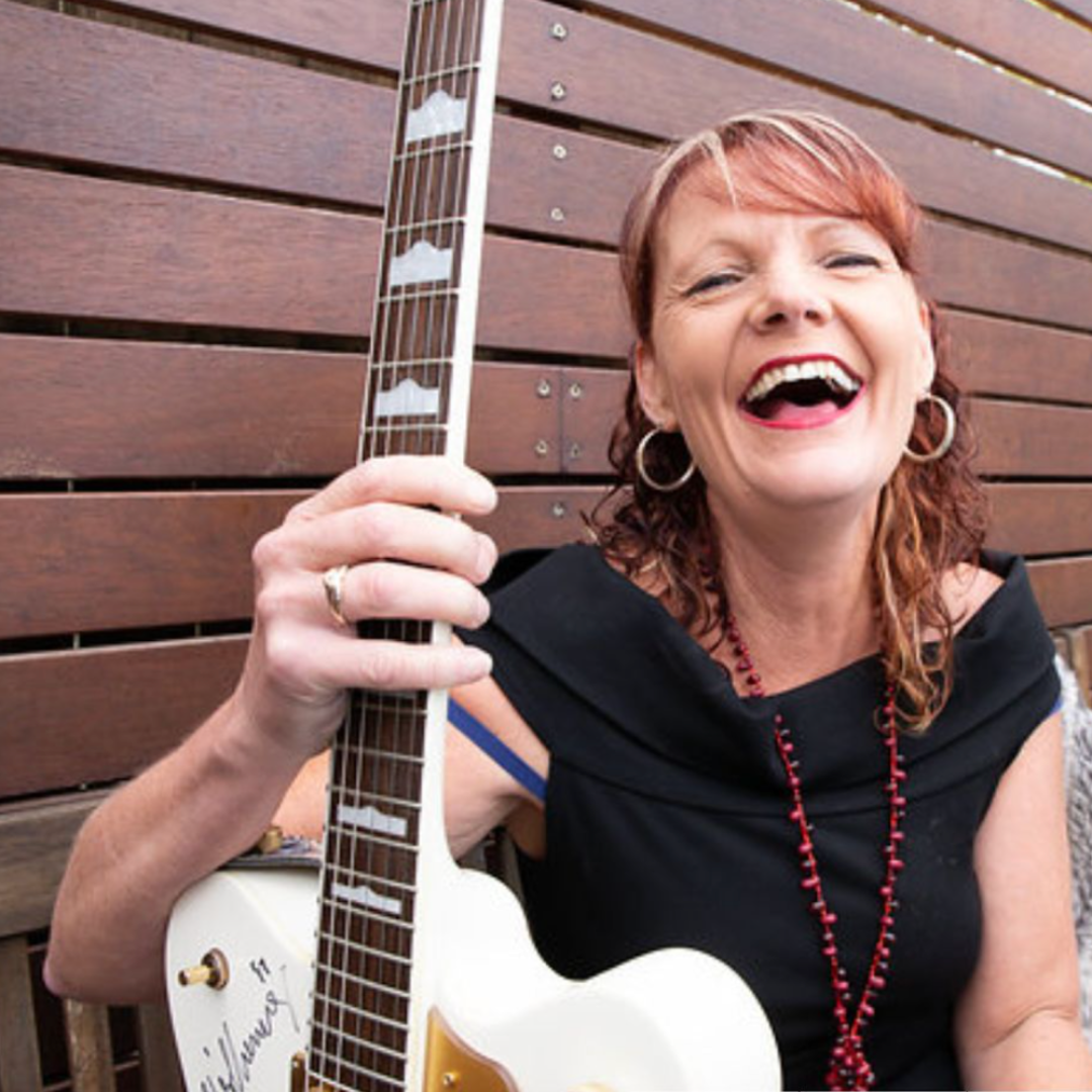 A Woman in A Black Dress Is Holding a White Guitar and Smiling — Chop 'n Chill in Port Macquarie, NSW