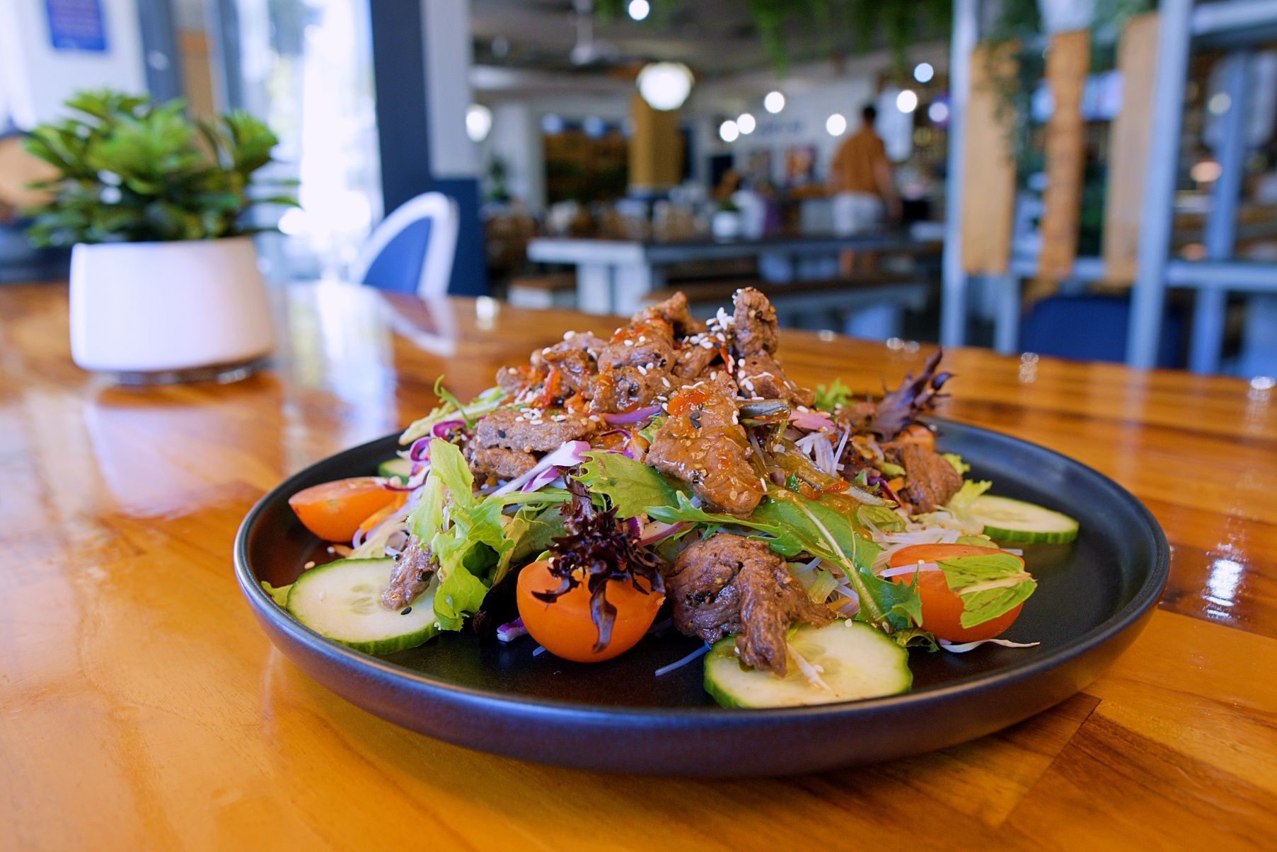 Salad With Sliced Meat, Vegetables, and Sesame Seeds on a Black Plate, Set on a Wooden Table — Chop 'n Chill in Port Macquarie, NSW